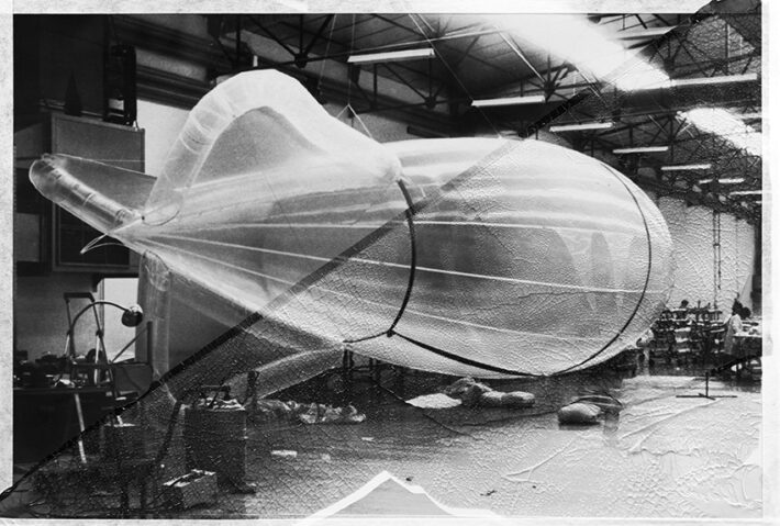 Structure gonflable translucide en forme d’aéronef dans un atelier, avec des effets de texture sur l’image en noir et blanc.