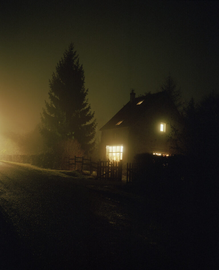 Paysage de nuit, une maison dans la brume, près d'un grand sapin. Les fenêtres sont éclairées.