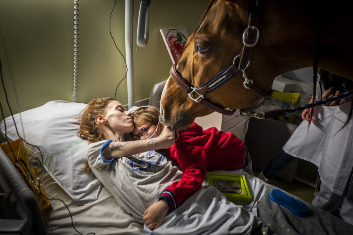 Un cheval visitant une femme à l'hôpital, accompagné d'un enfant et d'un soignant.